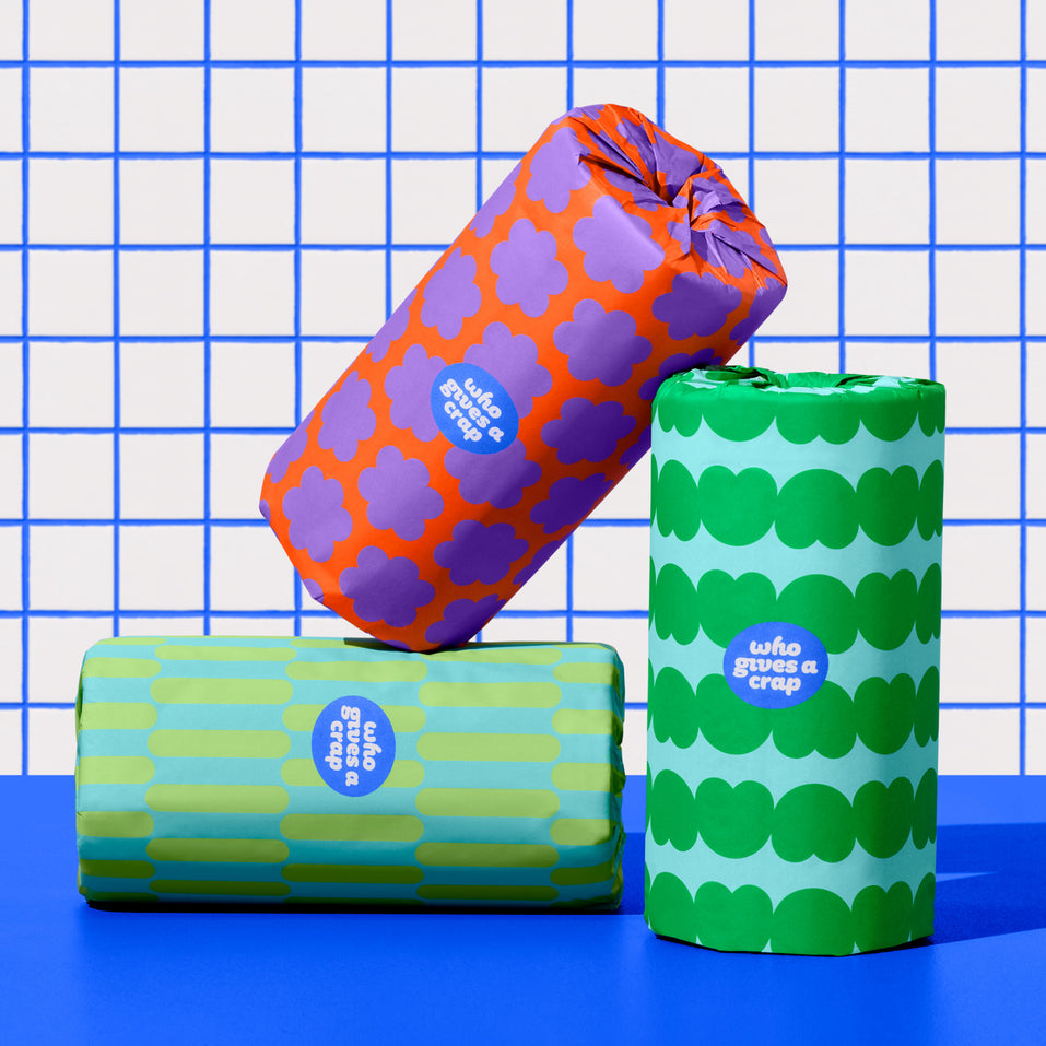 Three rolls of Who Gives a Crap kitchen roll against blue and while bathroom wall