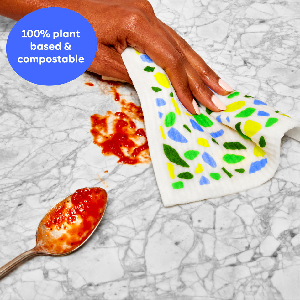 Hand using a plant based and compostable Swedish dish cloth to clean up a red tomato sauce mess on a countertop