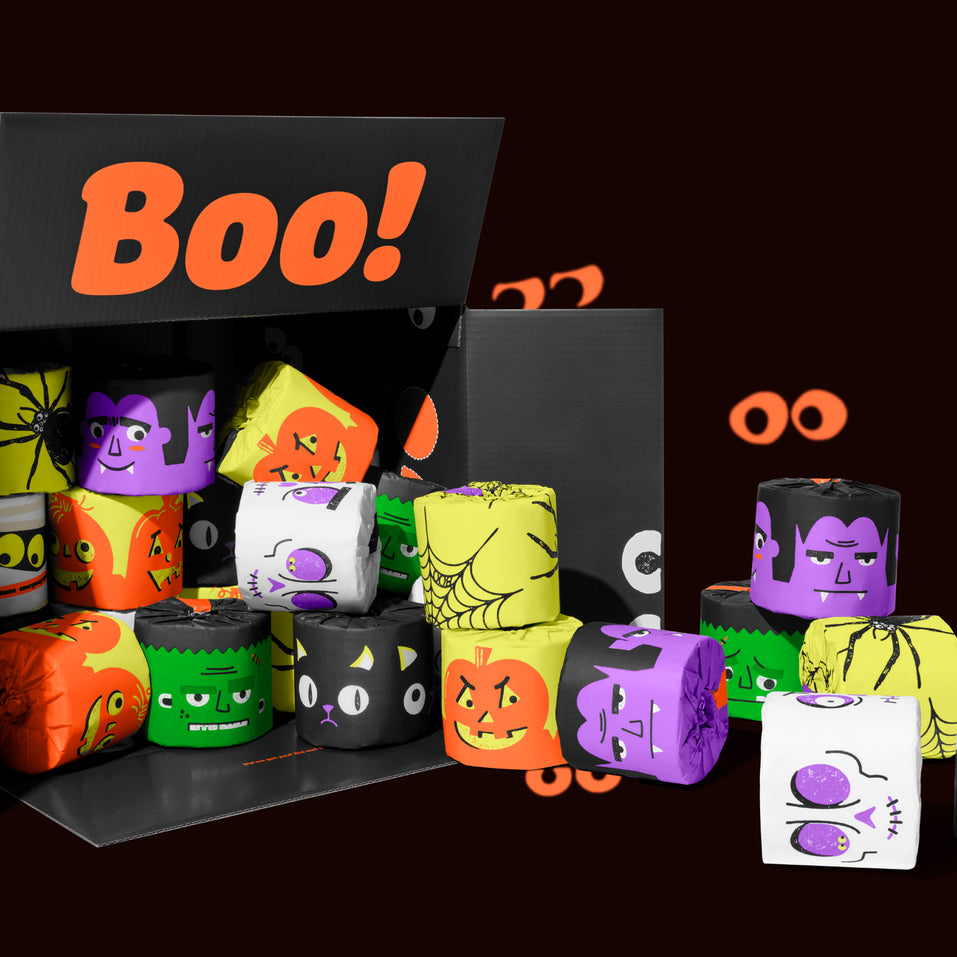 Open black box packed with Halloween-printed bamboo toilet paper rolls in orange, purple, green and white. Box reads 