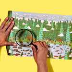Person using a magnifying glass to explore a flattened toilet paper roll illustrated with a forest scene on a yellow background
