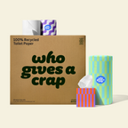 A Who Gives a Crap box with a paper towel, a tissue box, and two rolls wrapped in colourful packaging sitting on top