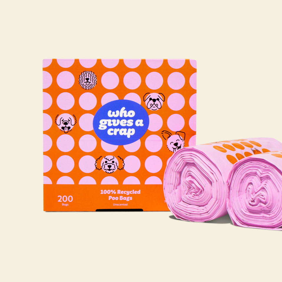 Two rolls of 100% recycled dog poo bags next to a orange and pink polka-dotted box that contains 200 bags.