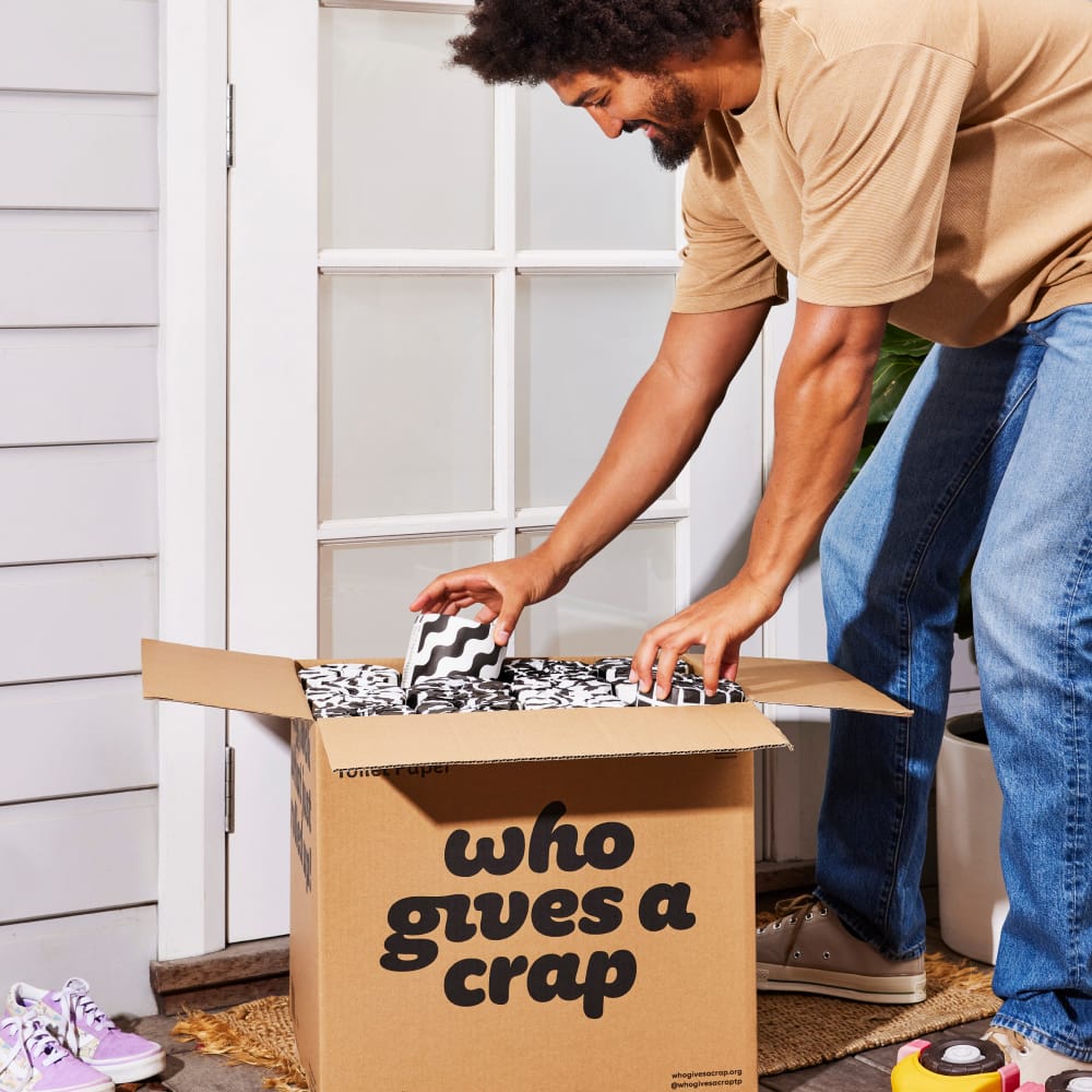 Person at front door with a delivery of a box of Who Gives A Crap toilet paper.