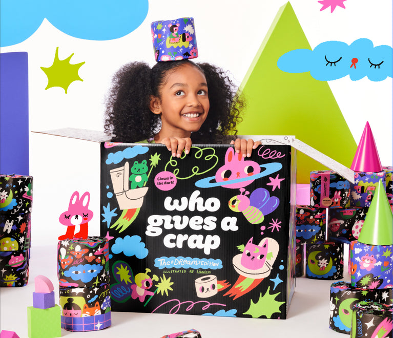 A child sitting inside a box of Dream Edition toilet paper surrounded by stacks of colourfully wrapped rolls and fun illustrative shapes and animals.