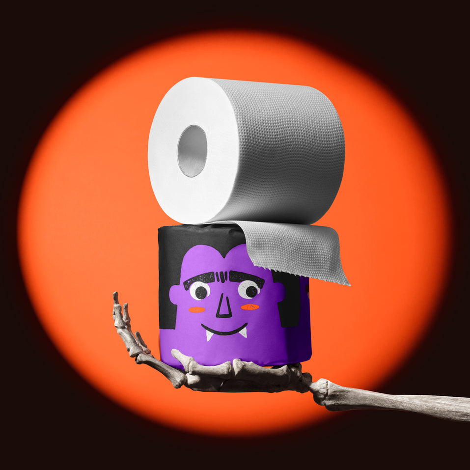 Skeleton hand holding a purple vampire roll of Spooky Edition bamboo toilet paper, unravelling in an orange spotlight