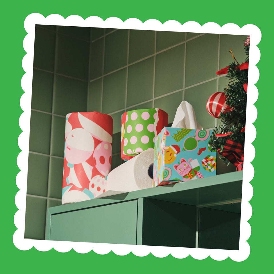 Wrapped Perfect Pair paper towel rolls and a tissue box on a green-tiled shelf with Christmas baubles.