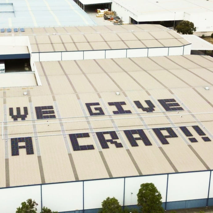 A large industrial building with letters on the roof made out of solar panels that reads "WE GIVE A CRAP!!" 