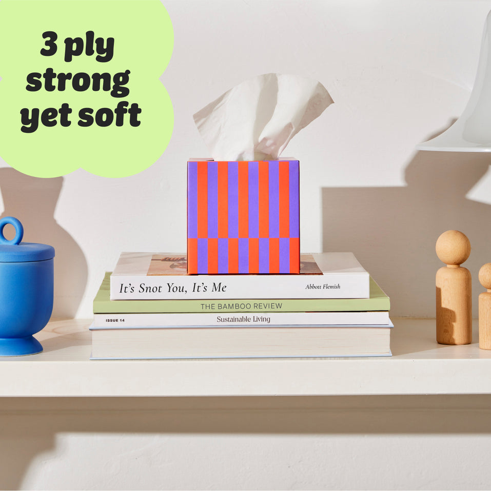 Who Gives a Crap tissue box sitting on a shelf atop a pile of book, with a caption reading ‘3 ply strong yet soft’