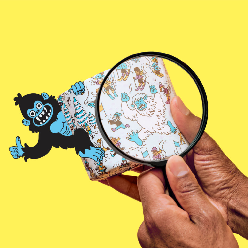 Hand holding a magnifying glass over a patterned toilet paper roll with cartoon characters on a yellow background